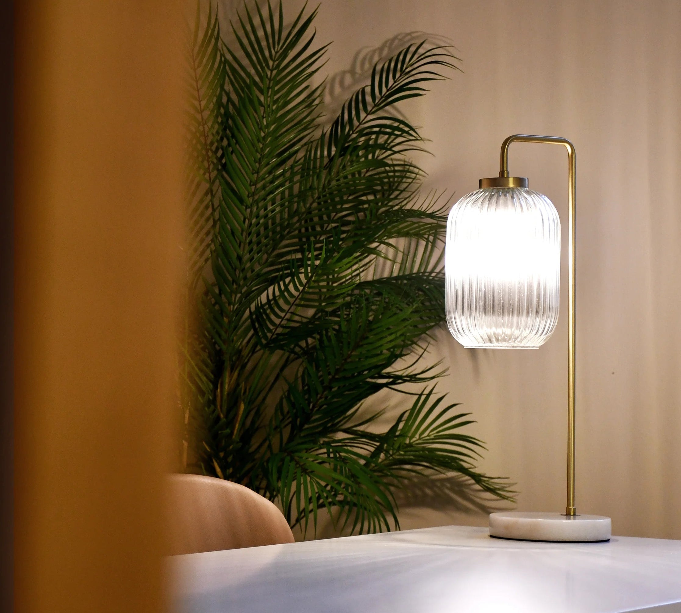 Modern table lamp with a decorative glass shade on a white surface, next to a plant.