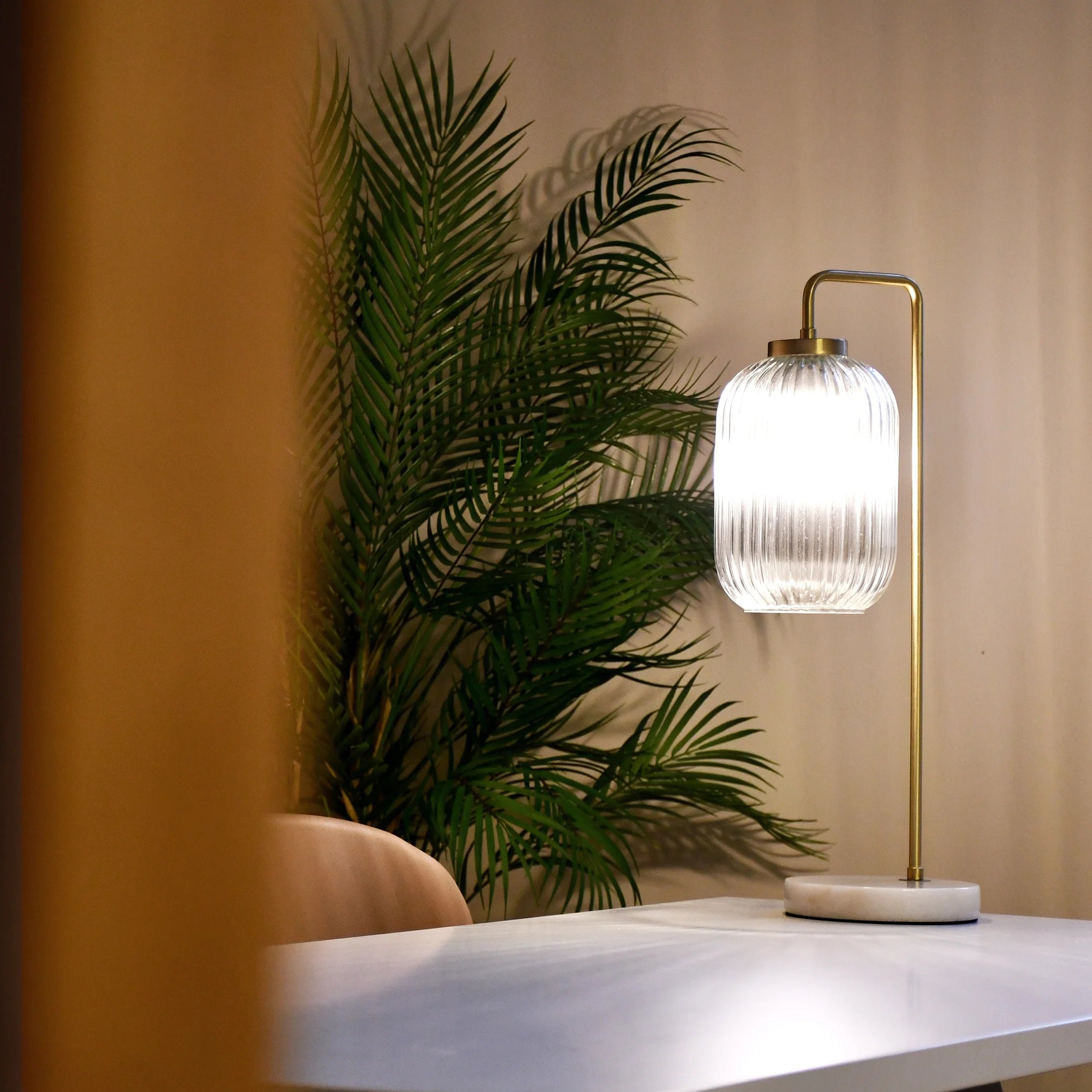 Modern table lamp with a decorative glass shade on a white surface, next to a plant.